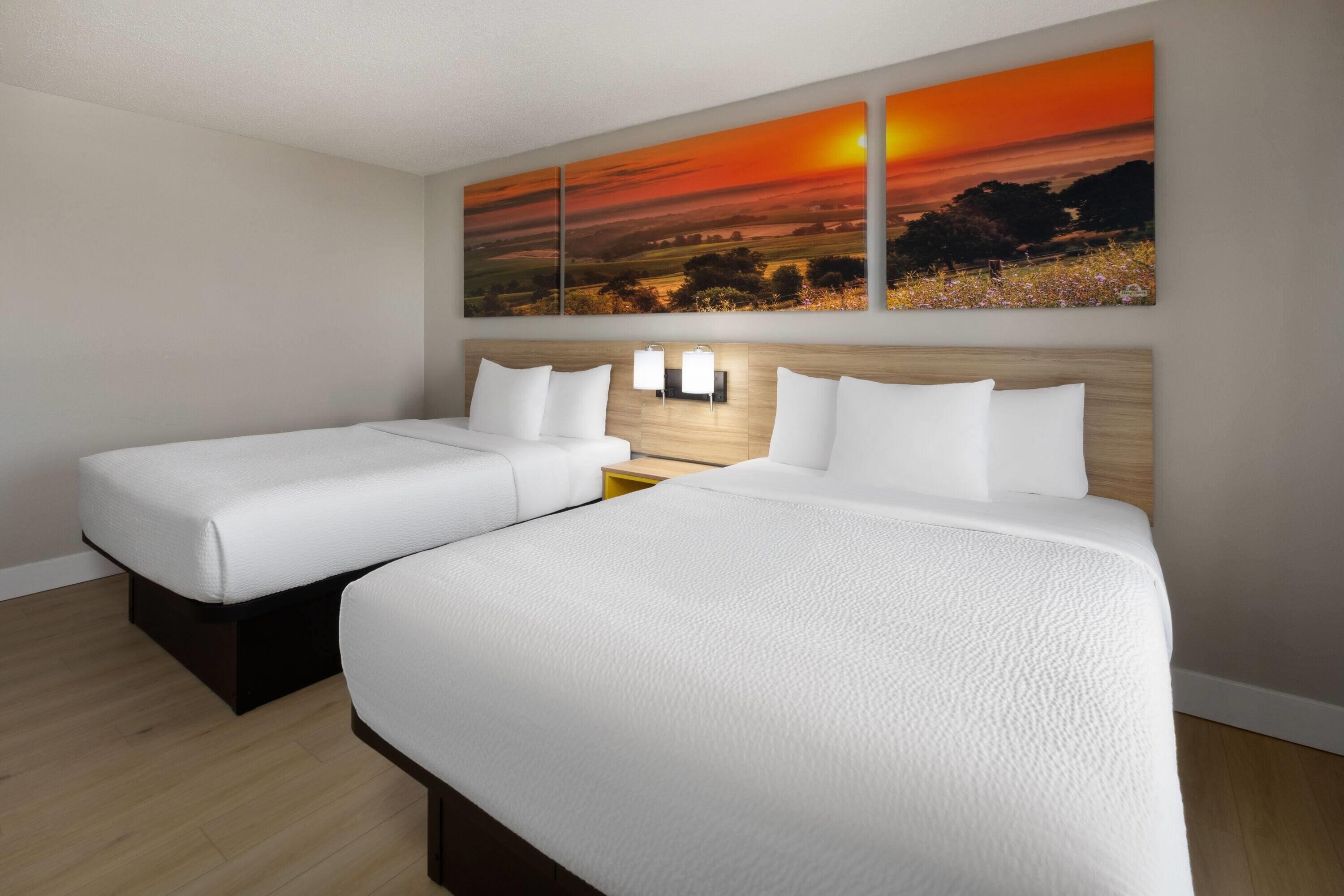 A hotel room with two beds, a wooden headboard, and a sunset painting on the wall.