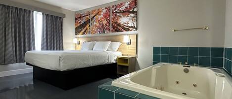 Habitación de hotel con cama, mesita de noche, lámpara de pared, ventana grande con cortinas y bañera con azulejos color turquesa.
