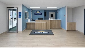 Zona de recepción de Days Inn con un mostrador de madera, puerta de vidrio de entrada y pared azul con el logotipo del hotel.