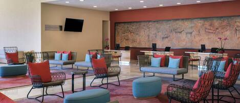 A hotel lobby with seating areas, a reception desk, and a large wall mural.