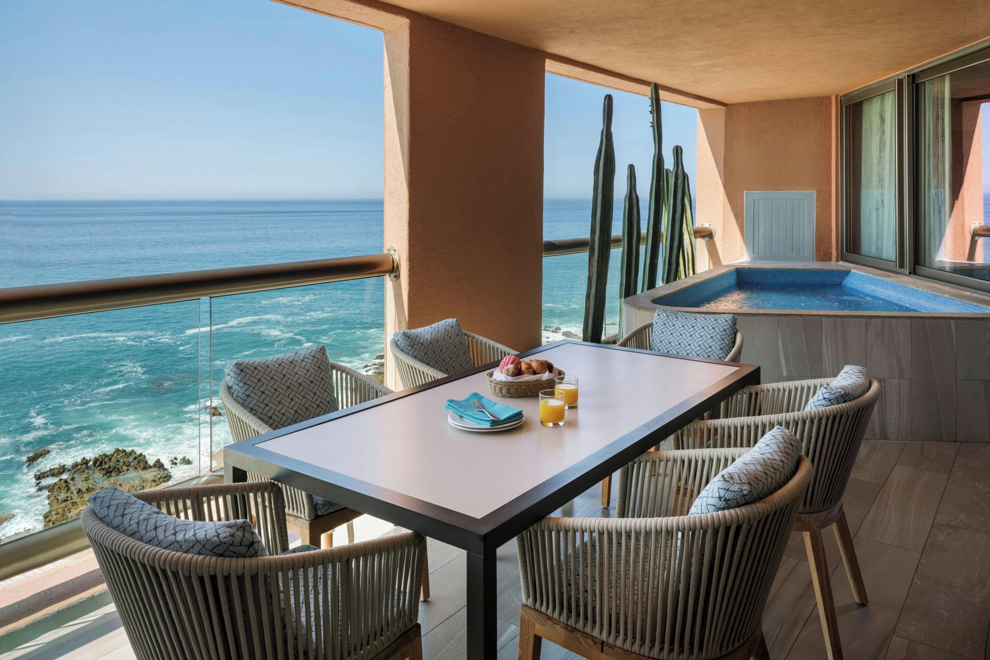 Un balcone con tavolo, sedie e vasca idromassaggio con vista sull'oceano.