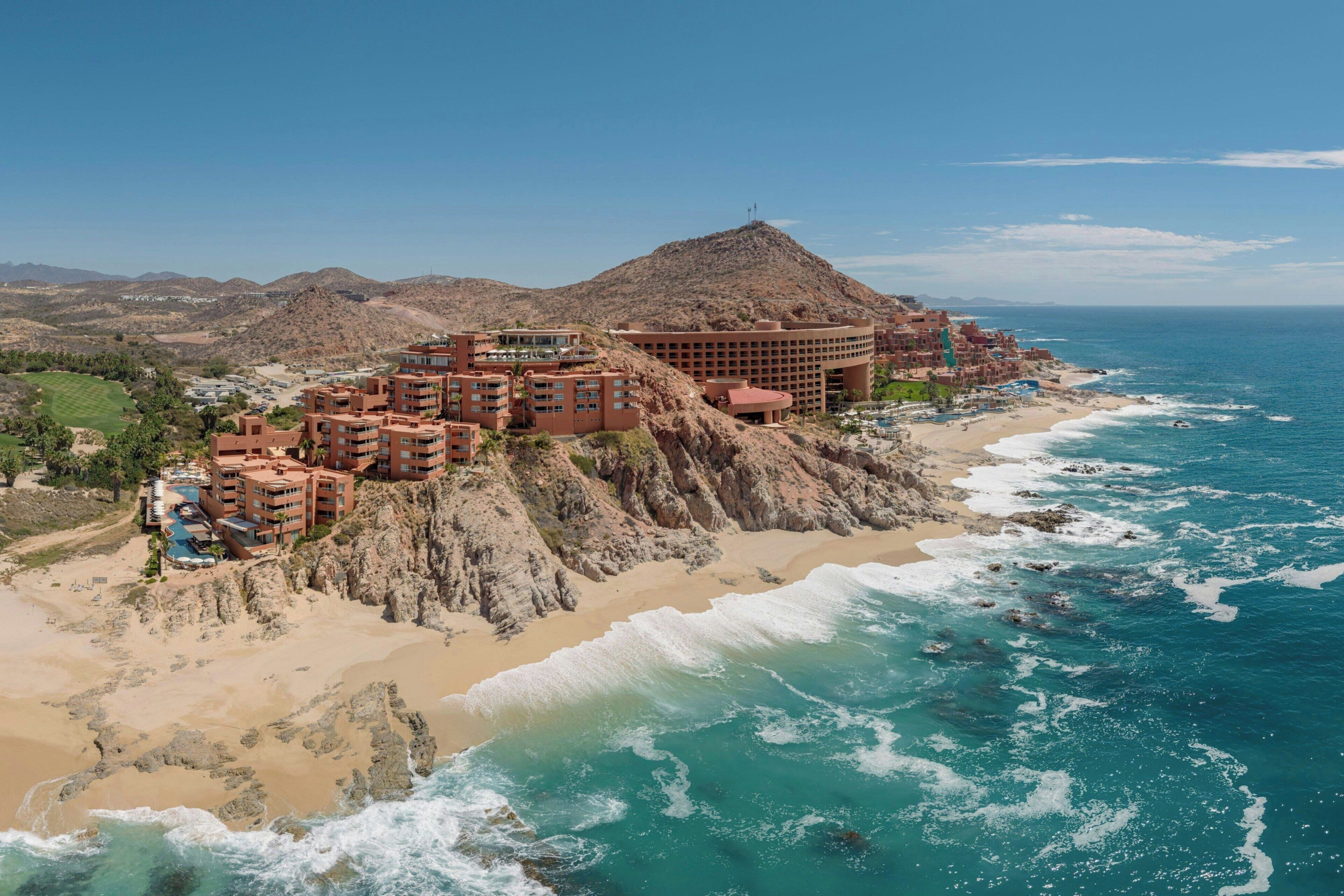 Un hotel frente al mar con varias edificaciones, playa y vistas al océano.