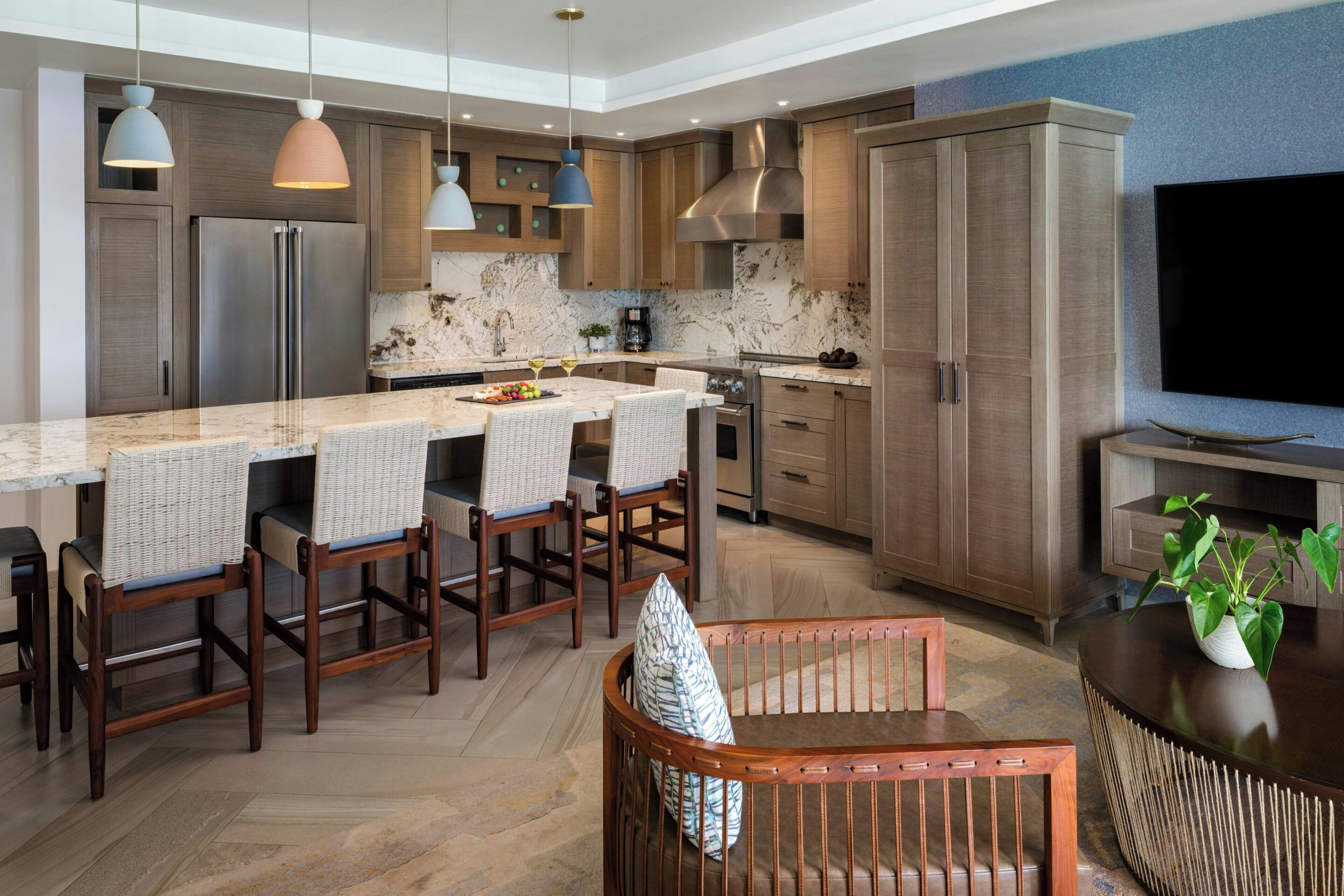 A modern kitchen with a marble countertop, wooden cabinets, and a large TV.