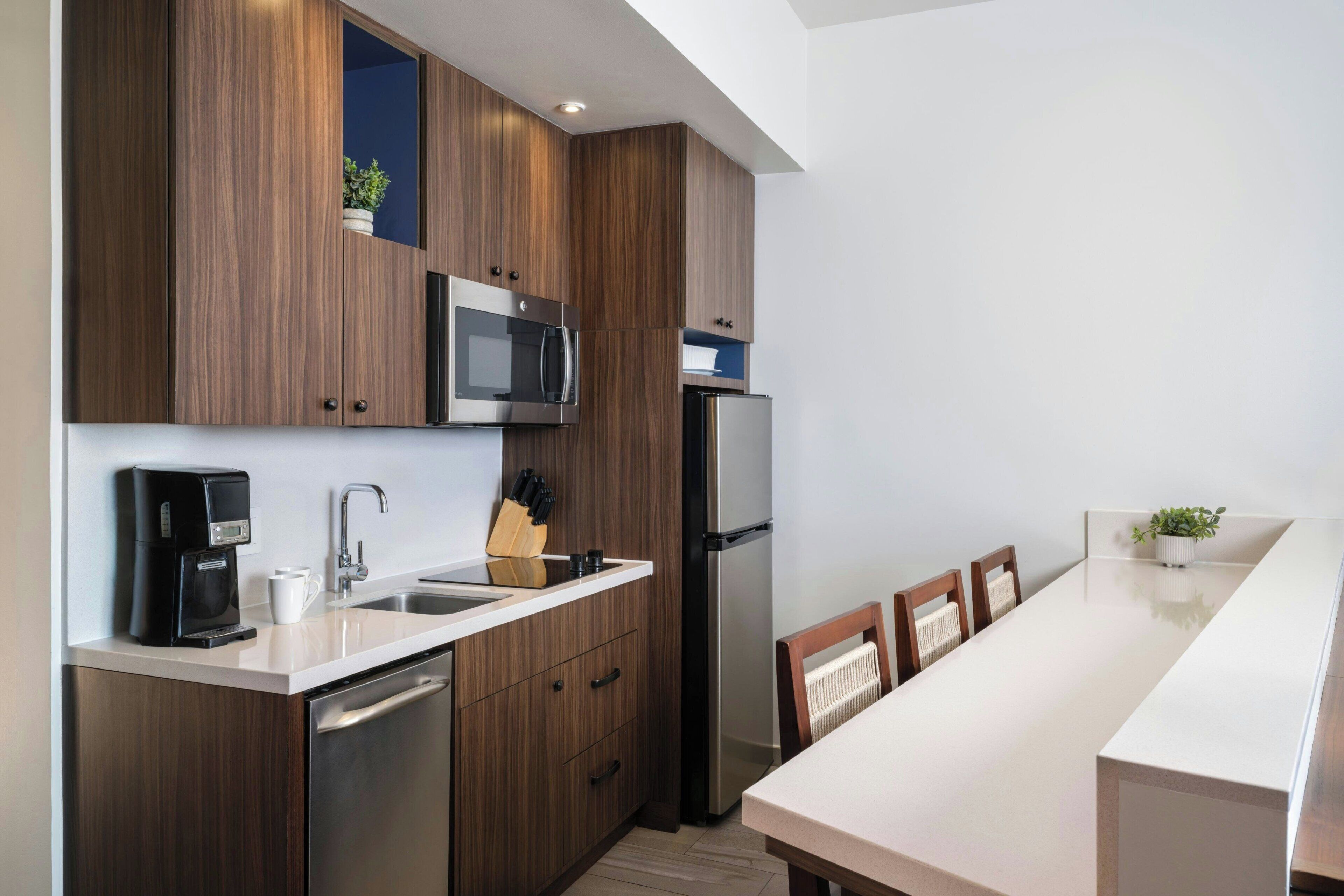 Een moderne keuken met houten kastjes, roestvrijstalen apparatuur, een koffiezetapparaat, en een eethoek met een witte tafel en stoelen.