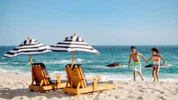 A beach with wooden lounge chairs and striped umbrellas.