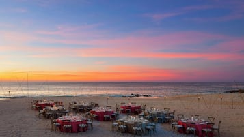 Montaje de comedor junto a la playa con mesas dispuestas para los huéspedes, con vistas al océano.