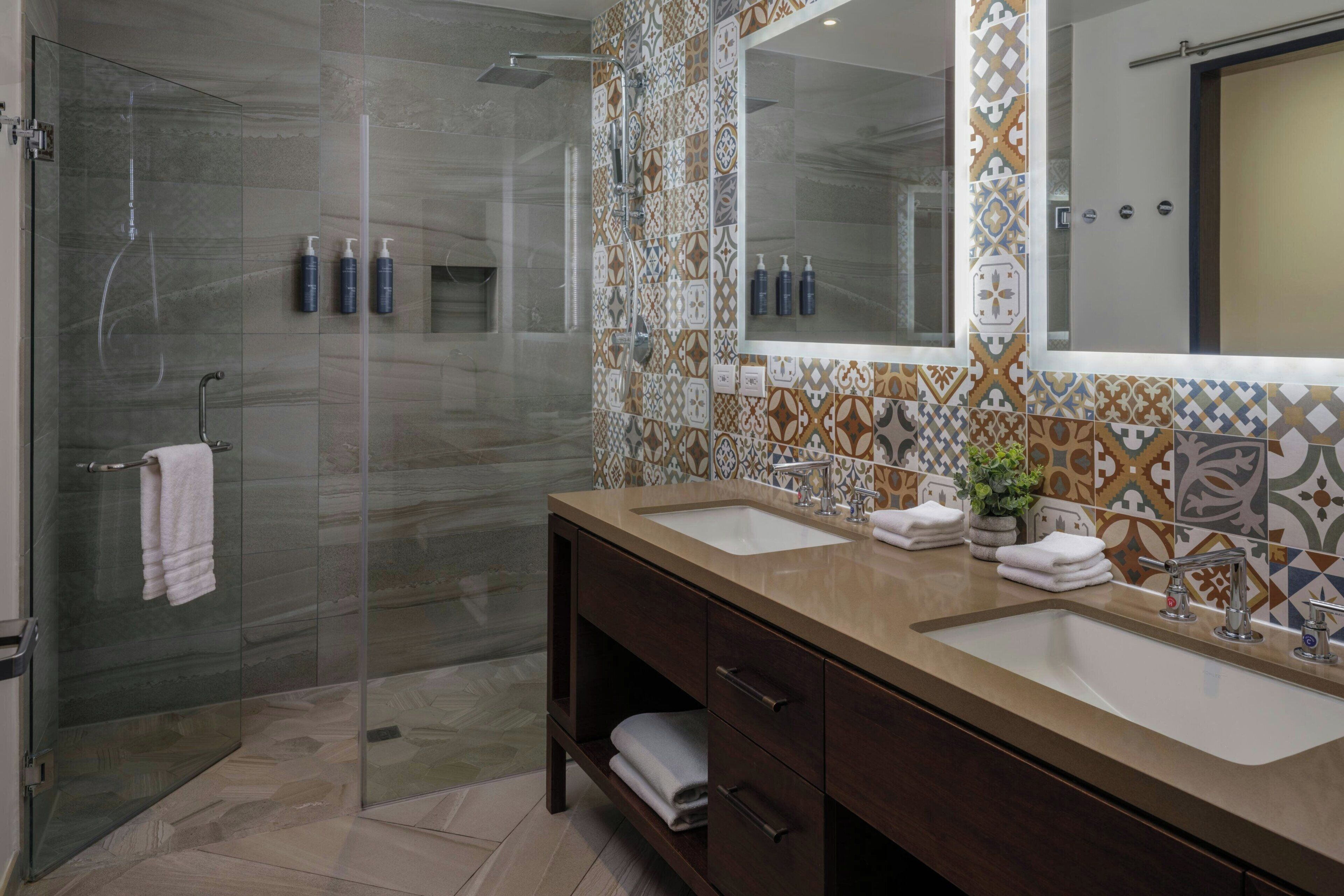 Une salle de bain moderne dotée d’une douche à parois de verre, de deux lavabos et d’un grand miroir.