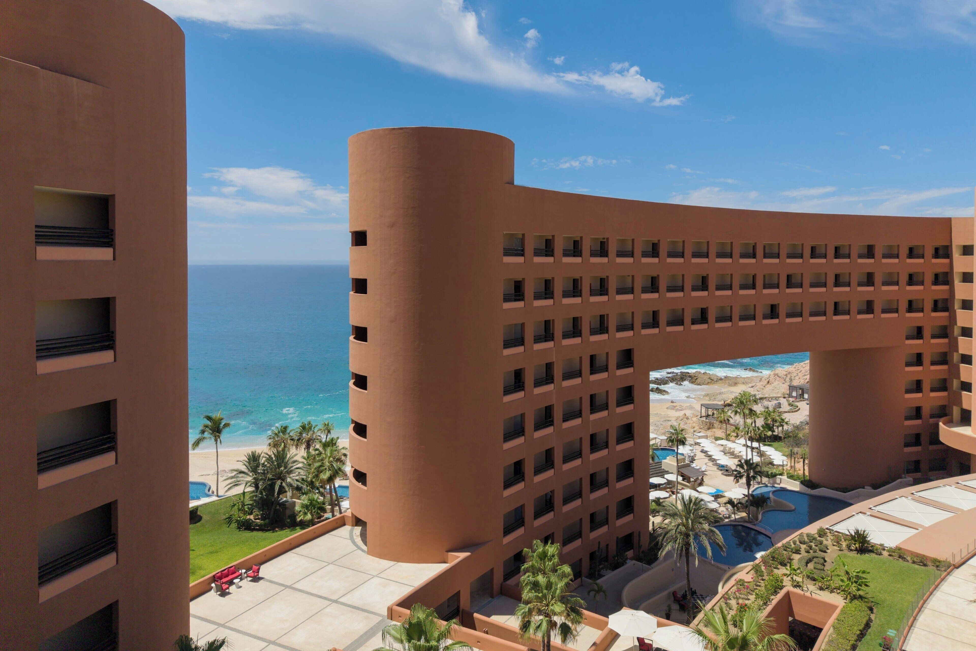 Un hôtel à la façade incurvée, donnant sur une plage et l’océan.