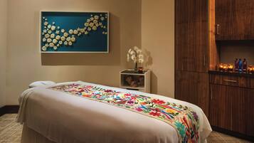 Habitación de hotel con una cama grande, un cuadro floral azul en la pared, una mesita de noche con un jarrón de flores blancas y armarios de madera.