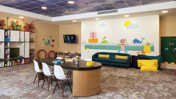 Children can play and relax in this vibrant play area with a round table, comfortable seating, and a colorful mural.