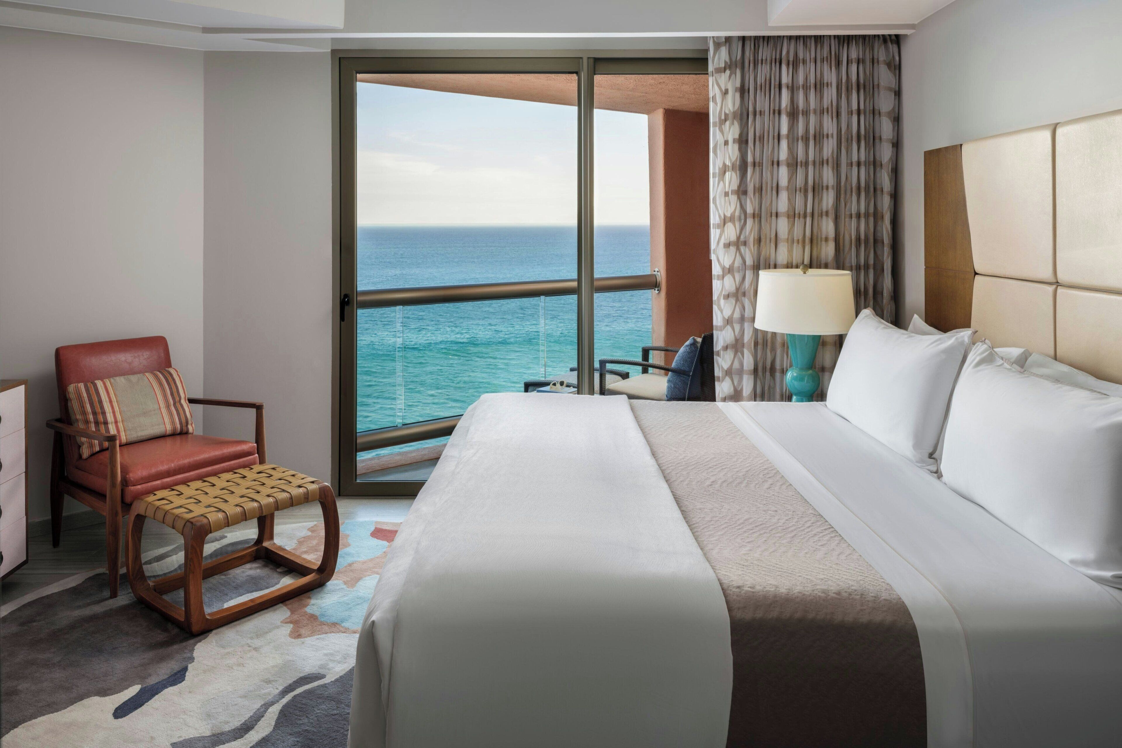 Ein Hotelzimmer mit einem großen Bett, einem Sessel, einem Schreibtisch und Blick aufs Meer.