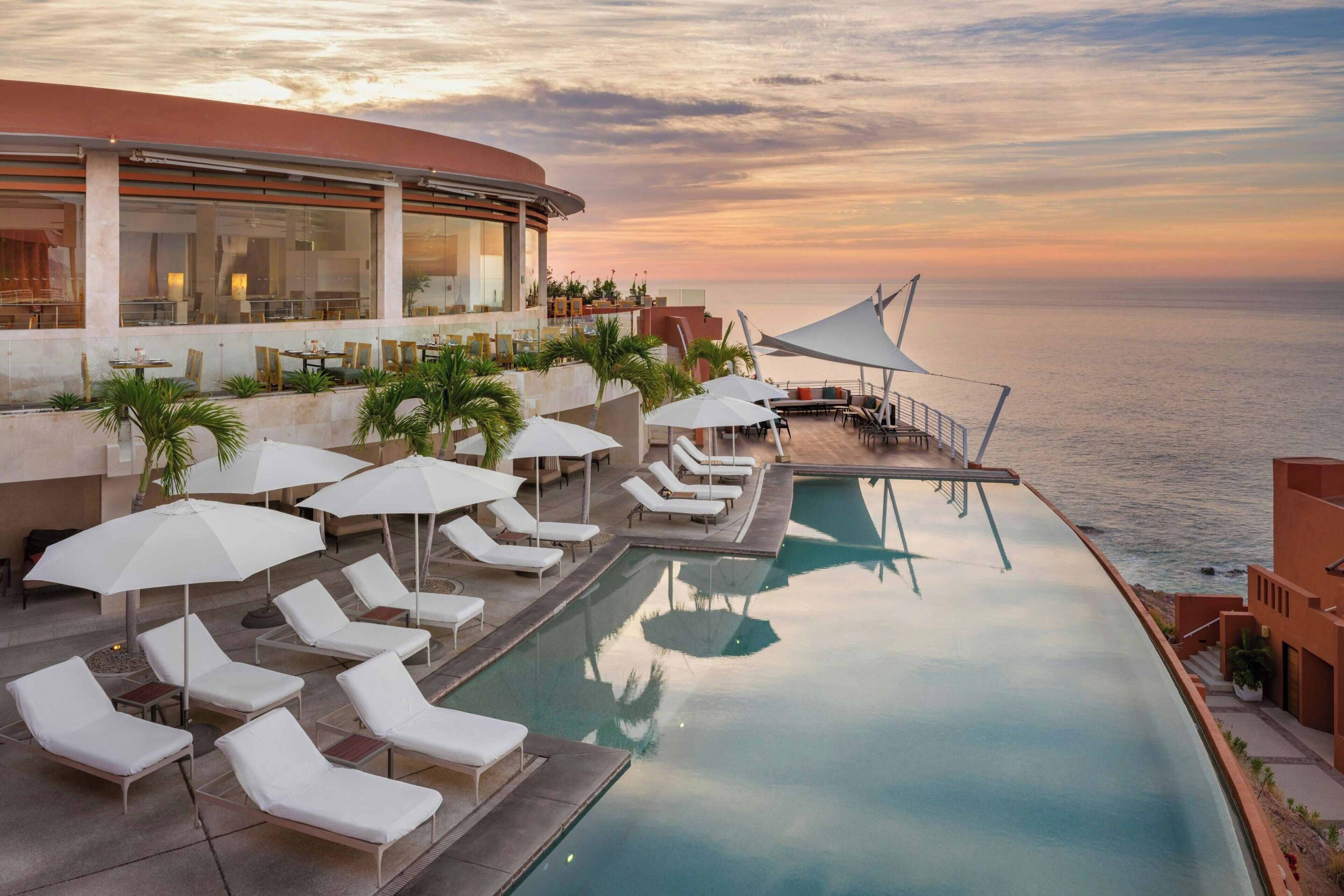 A poolside area with lounge chairs and umbrellas, overlooking the sea.