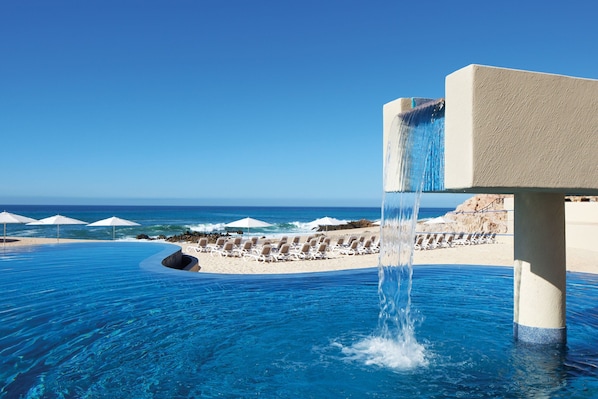 A infinity pool with a waterfall feature, beach chairs, and umbrellas. - The Westin Los Cabos Resort Villas (San José del Cabo)