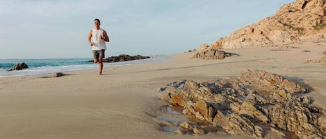 Una persona corrent a una platja sorrenca amb roques i un cel serè.