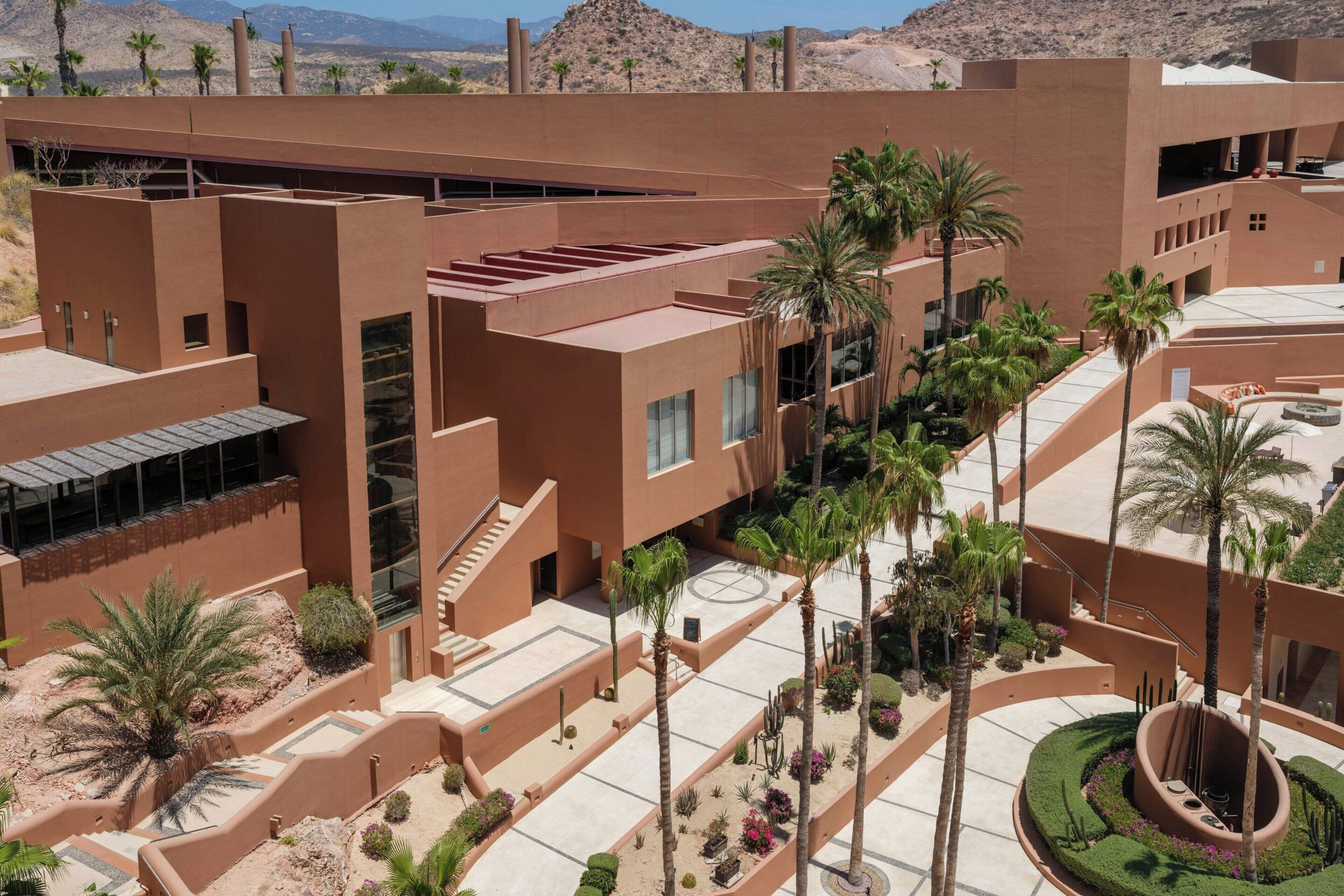 A modern building with multiple levels, outdoor terraces, and palm trees.