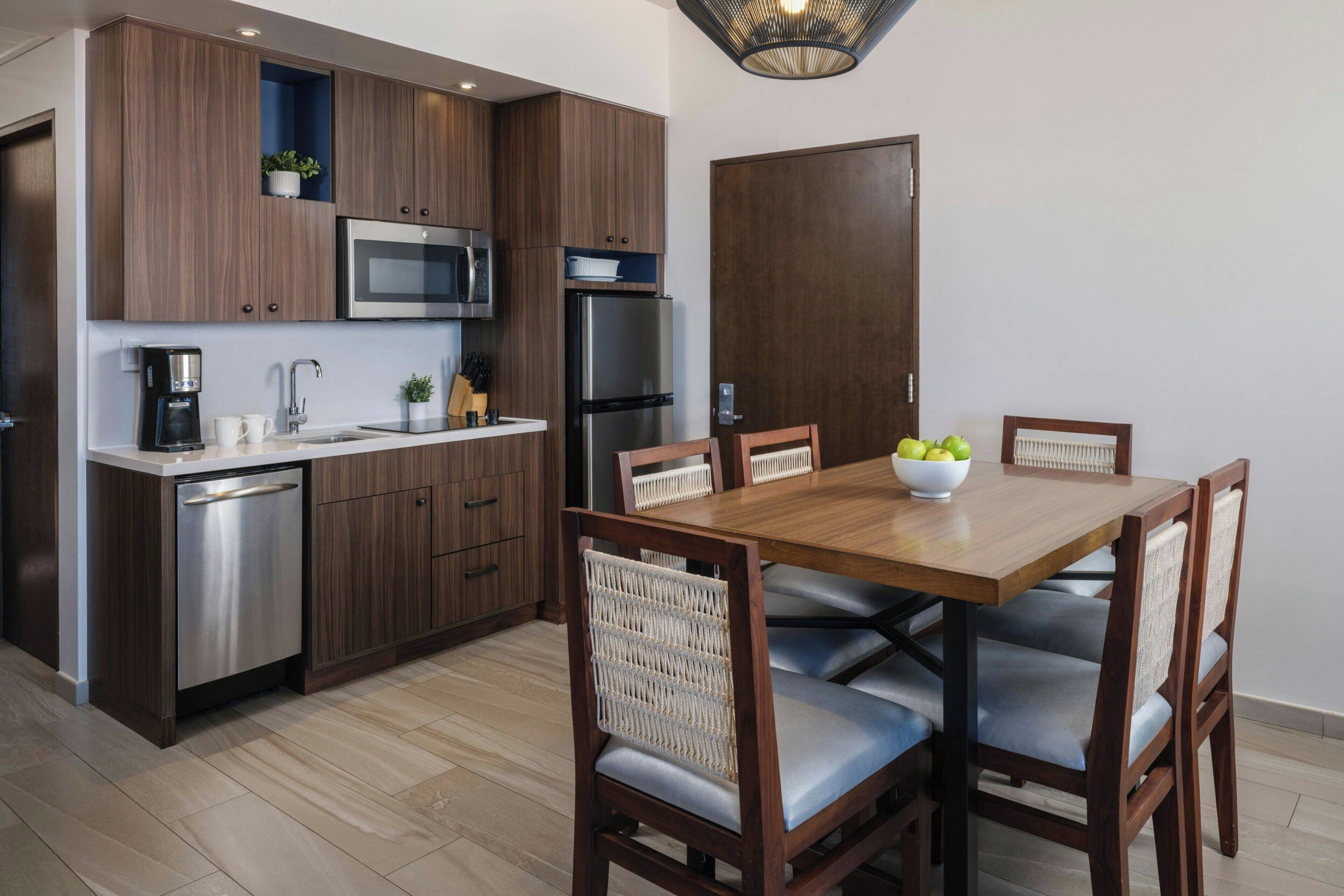 A modern kitchen with dark wood cabinets, stainless steel appliances, a built-in microwave, and a dining area with a wooden table and chairs.
