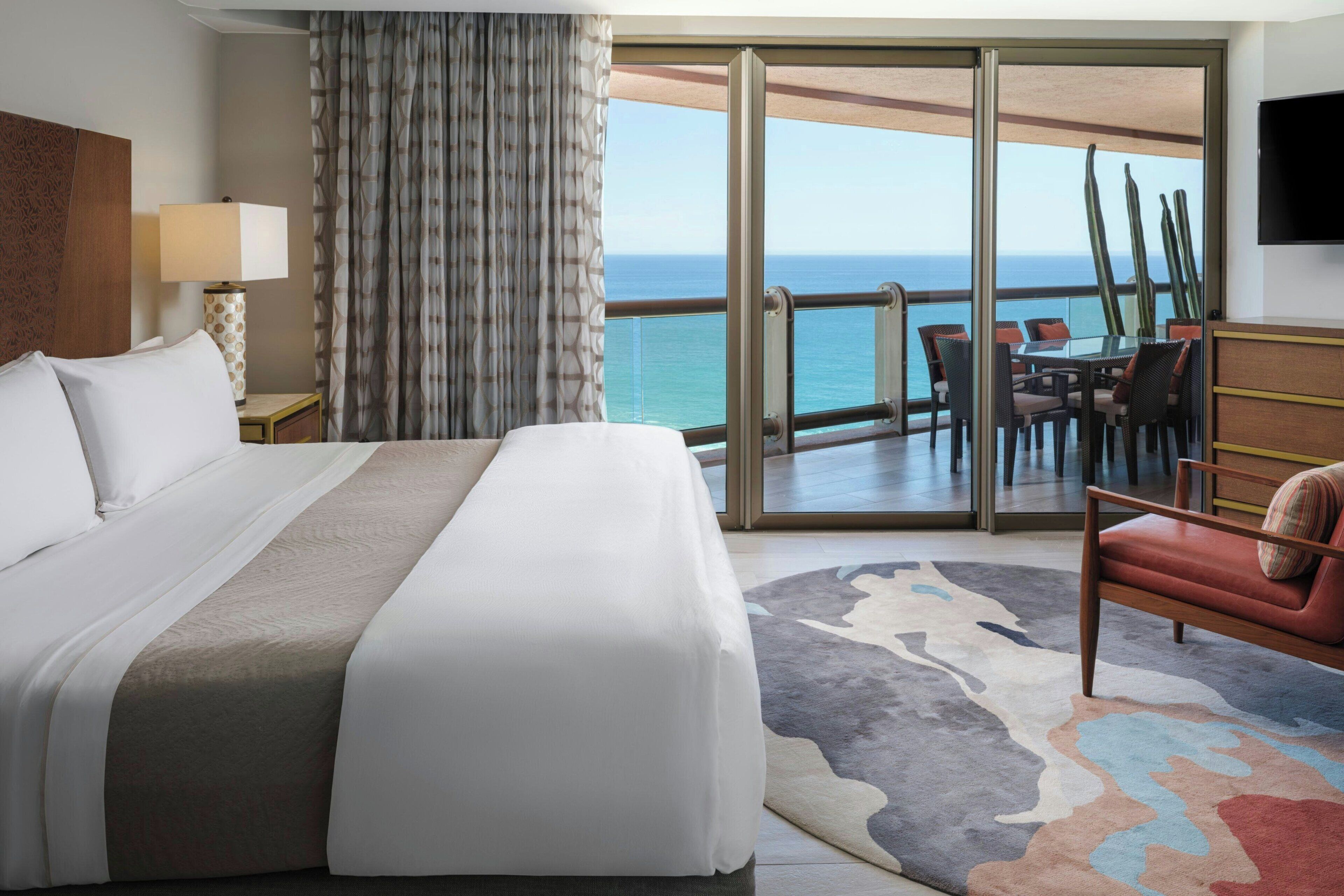 Een hotelkamer met een groot bed, uitzicht op zee, een balkon met buitenmeubilair en een flatscreen televisie.