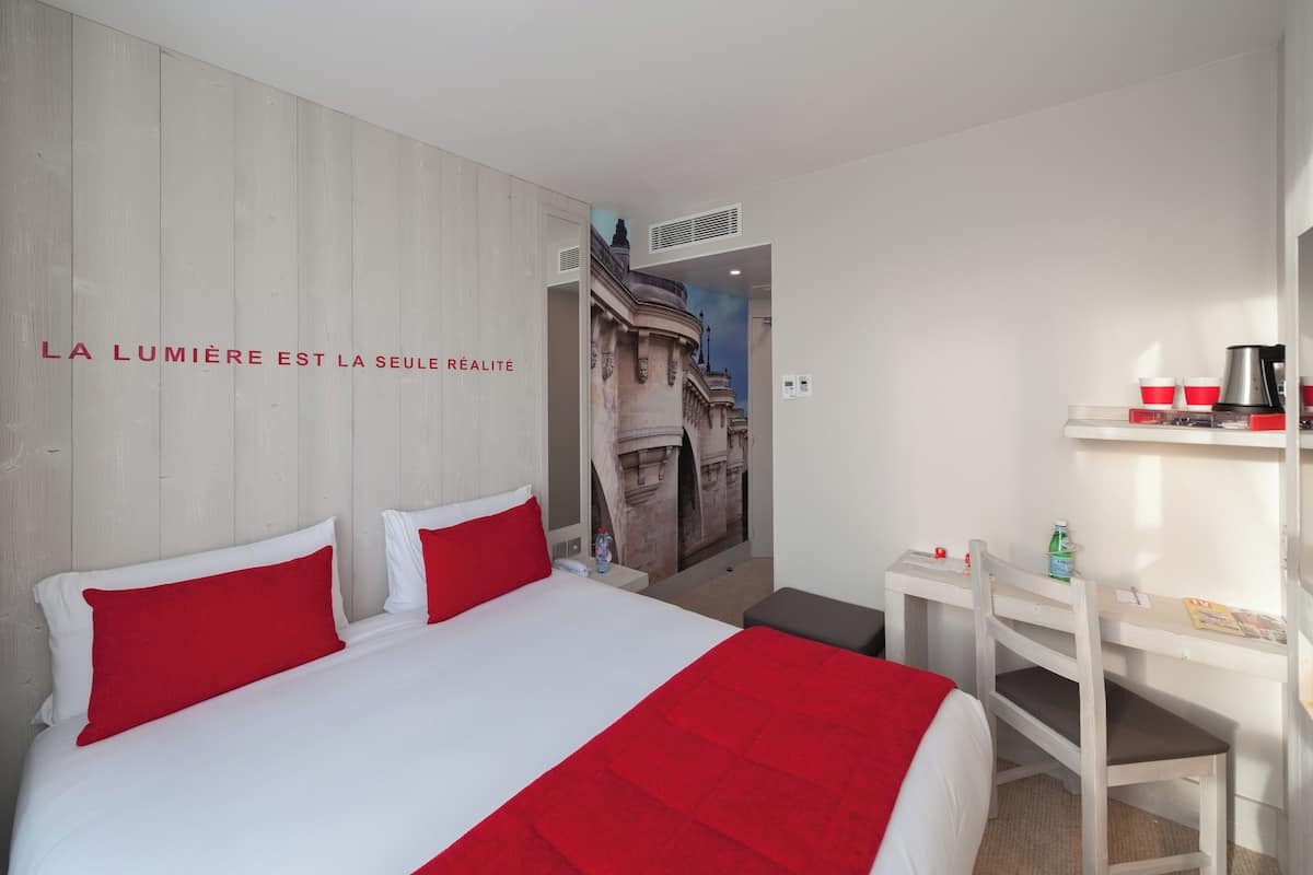 Une chambre d’hôtel avec un lit, un bureau et une étagère où se trouvent des tasses et une bouilloire.