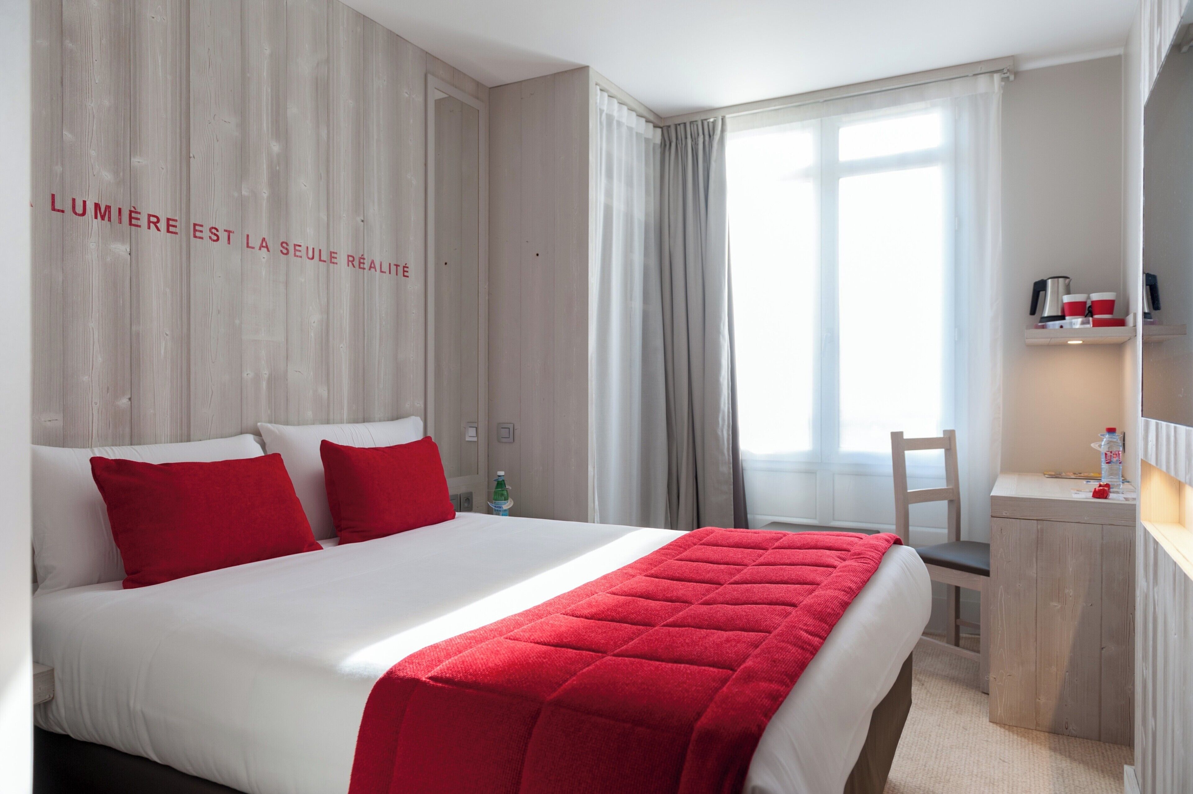 Habitación de hotel con cama, escritorio, silla y ventana con cortinas.