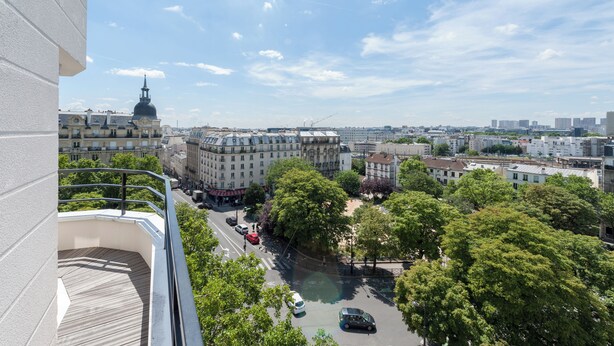 Un edificio alto con un balcón que da a un paisaje urbano, incluyendo una cúpula destacada y varios edificios.