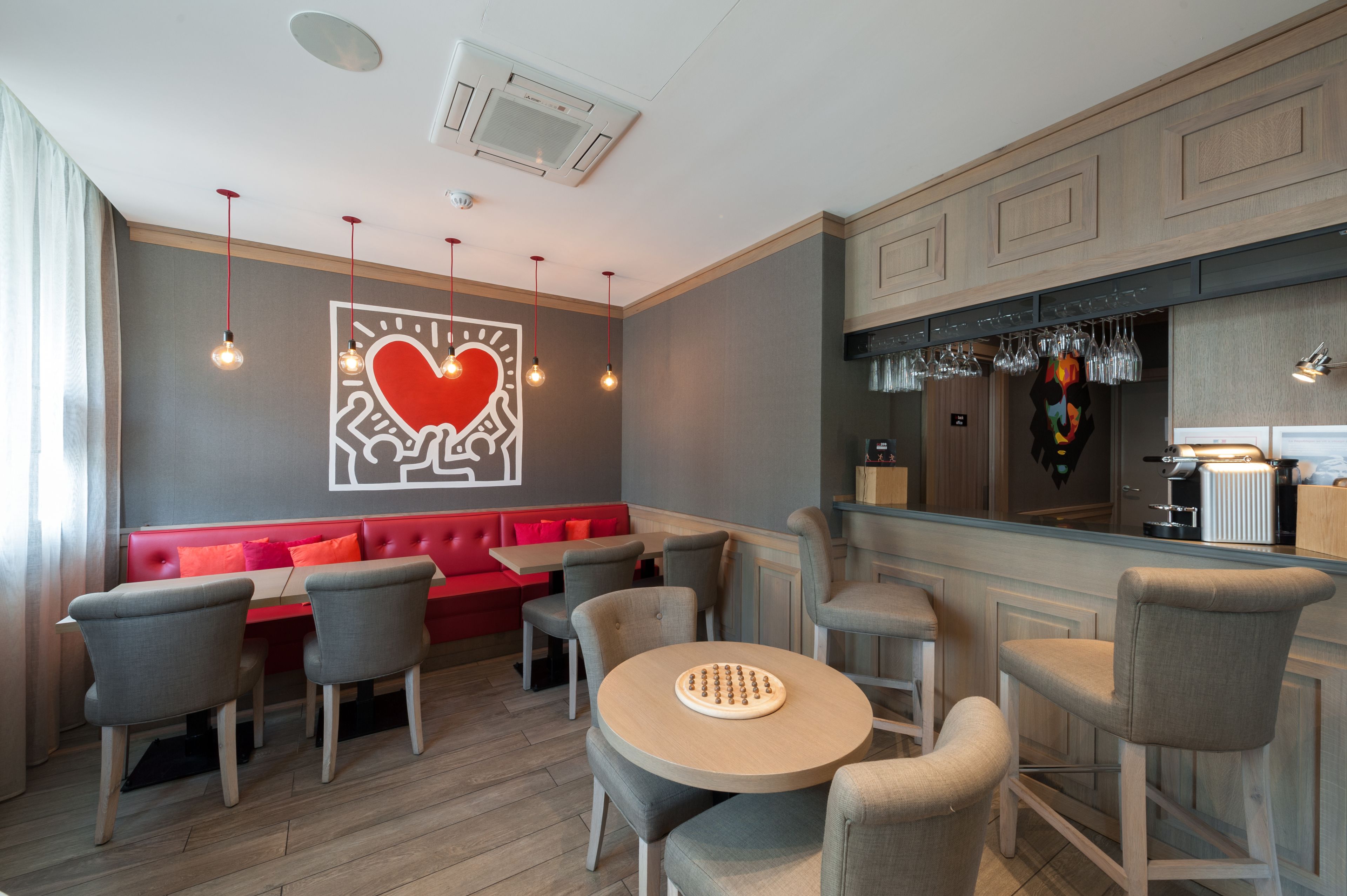 A restaurant with a red booth seating, grey chairs, and a round table.