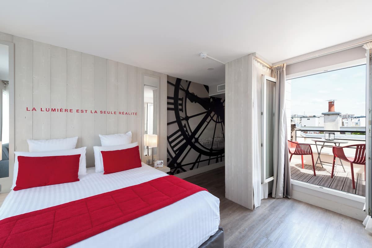 Une chambre d’hôtel avec un lit, une peinture murale représentant une horloge et un balcon avec des chaises.