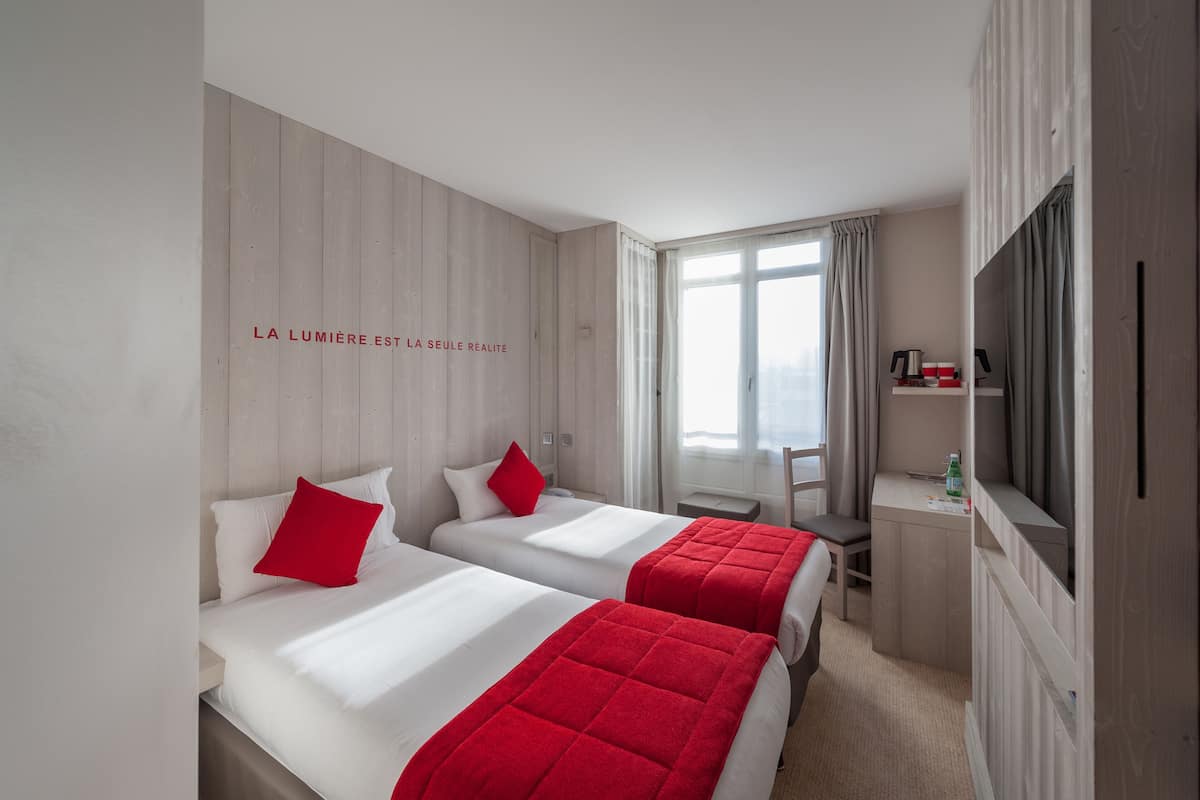 Une chambre d’hôtel avec deux lits, un bureau, une chaise, une télévision et une fenêtre avec des rideaux.