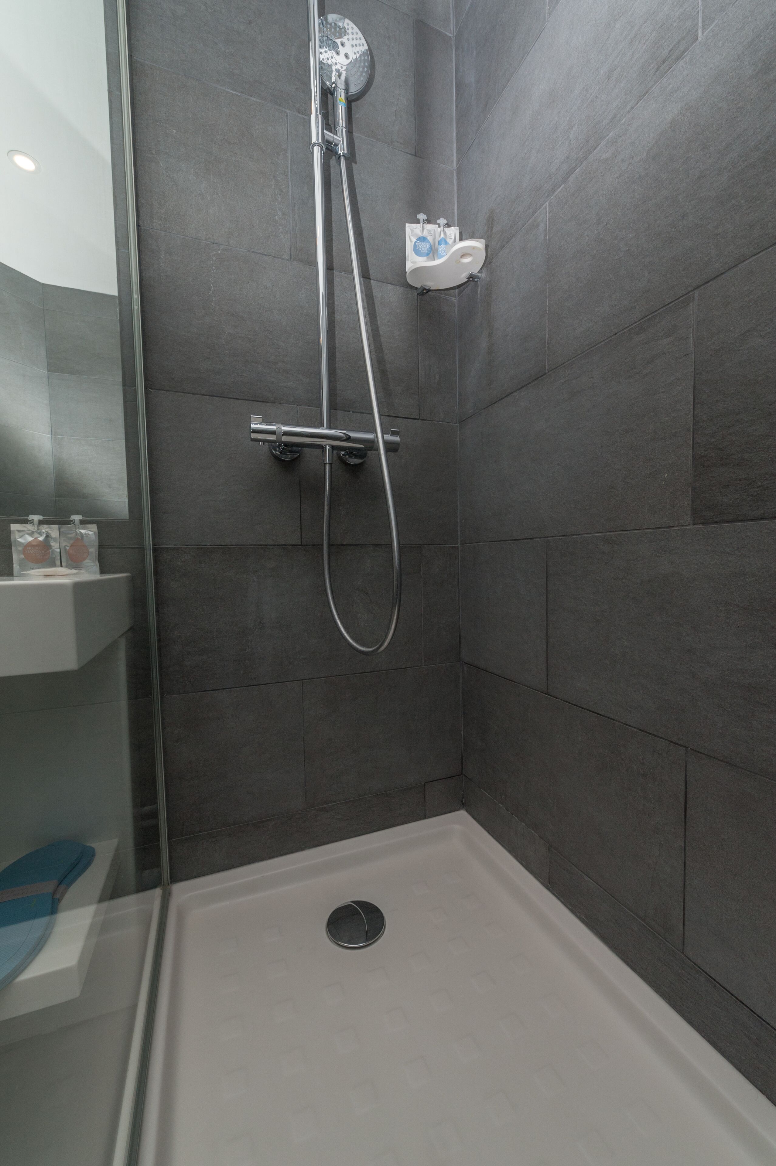 A shower area with a glass door, a handheld showerhead, and a wall-mounted faucet.