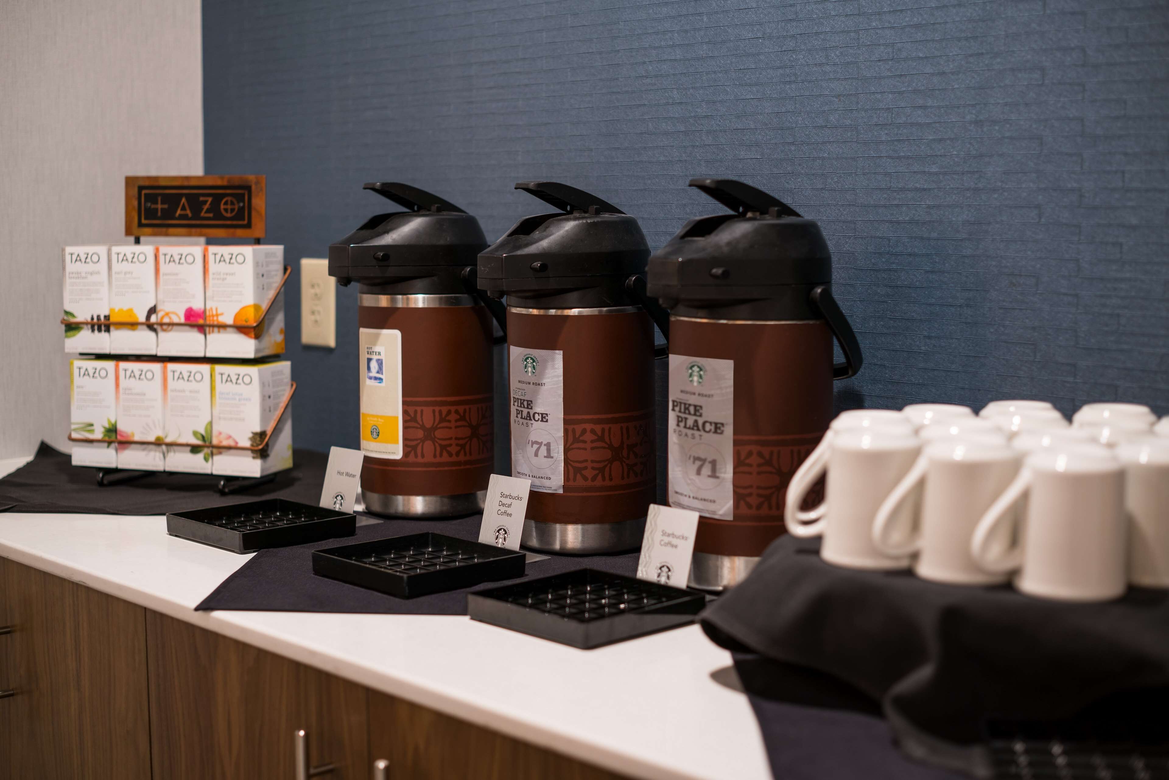 A coffee station with multiple coffee dispensers, a stack of coffee boxes, and a sign indicating the coffee type.