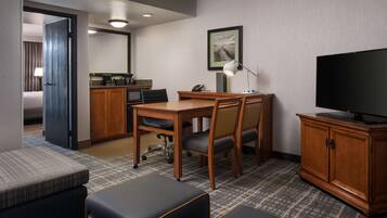 Hotelkamer met een houten bureau, twee stoelen, een televisie, een kast, een kleine kitchenette en een bed met uitzicht.