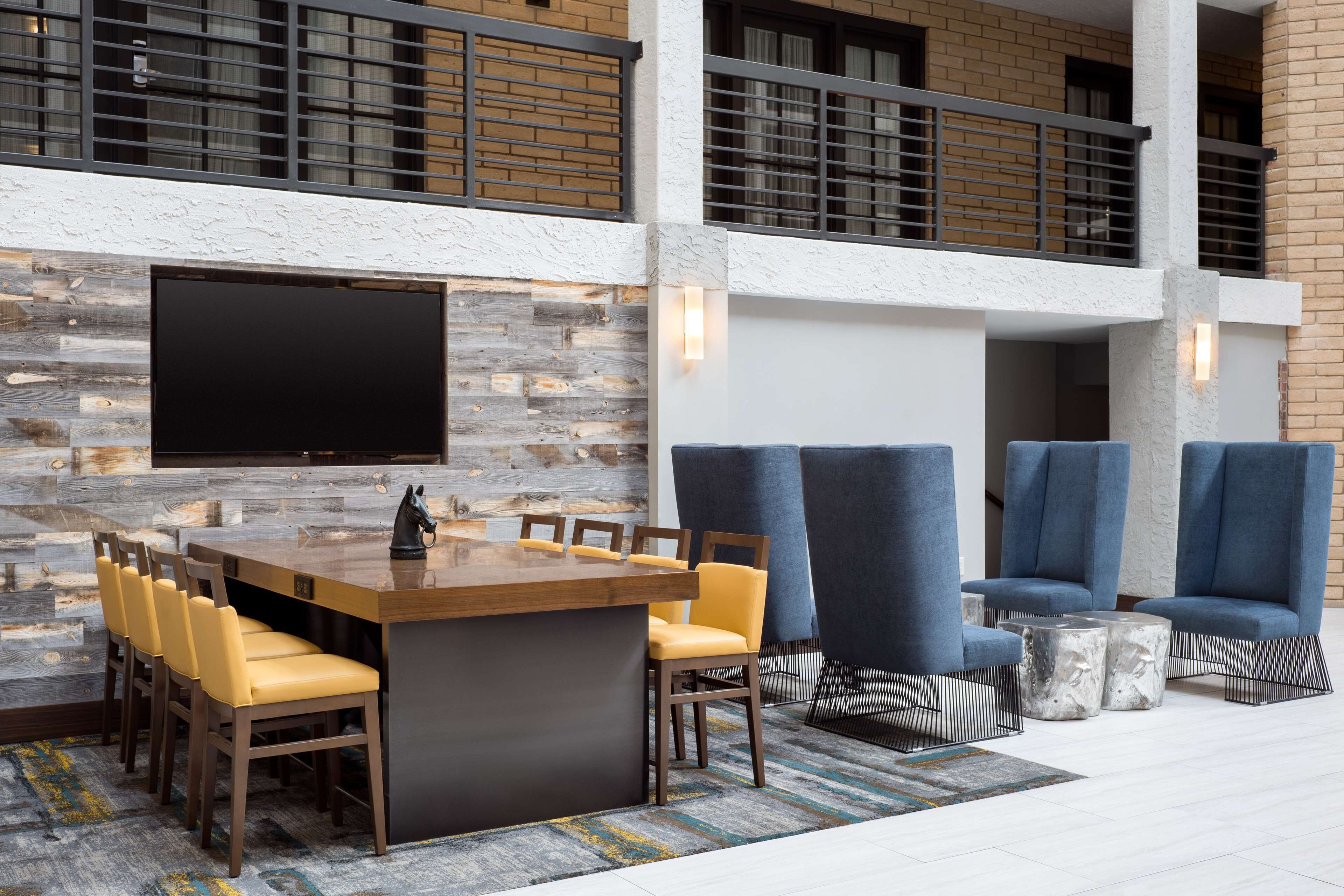 Ein moderner Loungebereich mit einem Holztisch und gelben Stühlen, einem großen Flachbildfernseher an der Wand und blauen Polsterstühlen mit Marmorschlauchtischen.