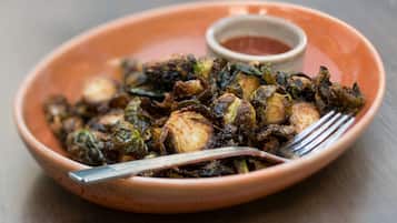 Un tazón de terracota con brócoli de Bruselas asado, acompañado de un recipiente pequeño con salsa y un tenedor.