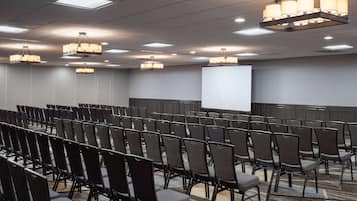 A conference room with rows of chairs, a projector screen, and multiple chandeliers.