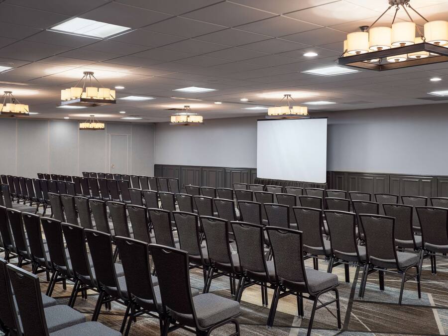 A conference room with rows of chairs, a projector screen, and multiple chandeliers.