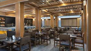Un restaurante moderno con vigas de madera, varias zonas de comedor y una barra con una pantalla grande.