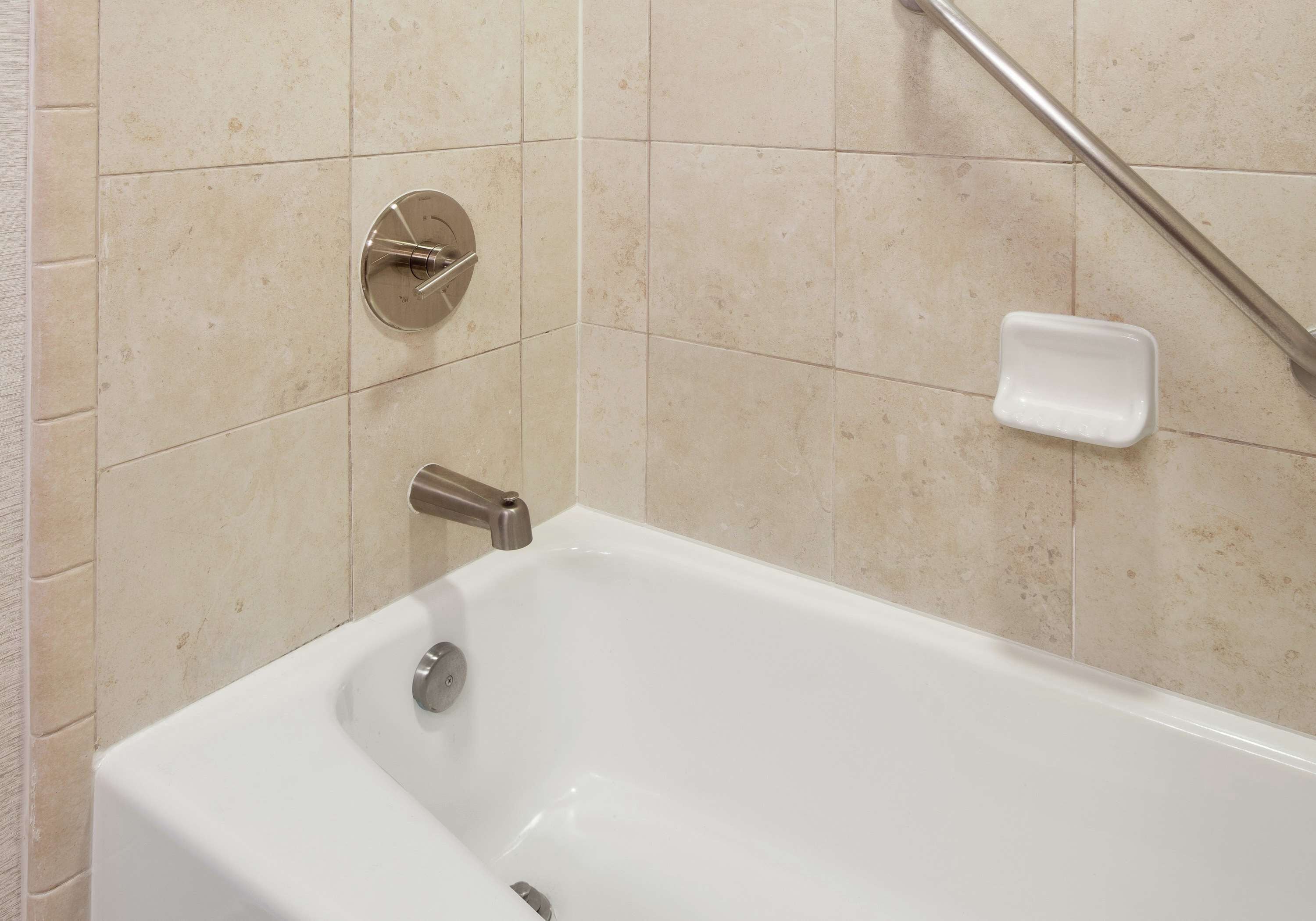 Una vasca da bagno bianca con un soffione a mano, un rubinetto montato sulla parete e un portasapone.