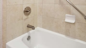 Una bañera blanca con ducha de mano, grifo empotrado en la pared y jabonera.