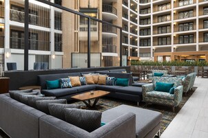 A modern hotel lobby with a grey sectional sofa, patterned armchairs, and a wooden coffee table.