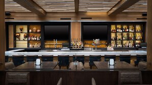 Zona de bar con techo de madera, estantes llenos de botellas y asientos.