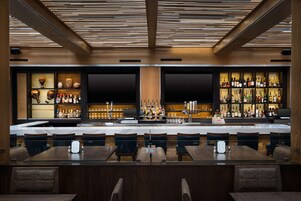 A bar area with wooden ceiling, shelves of bottles, and seating.