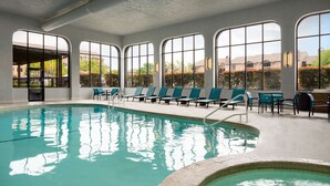Una piscina interior con agua cristalina, rodeada de sillas de descanso y grandes ventanales.