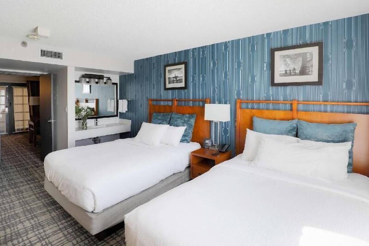 A hotel room with two beds, a bathroom, and a hallway.