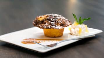 A dessert on a white plate with a fork, a muffin, whipped cream, and a mint garnish.
