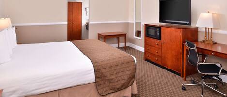Una habitación de hotel con una cama grande, un escritorio con silla, un televisor y un espejo.