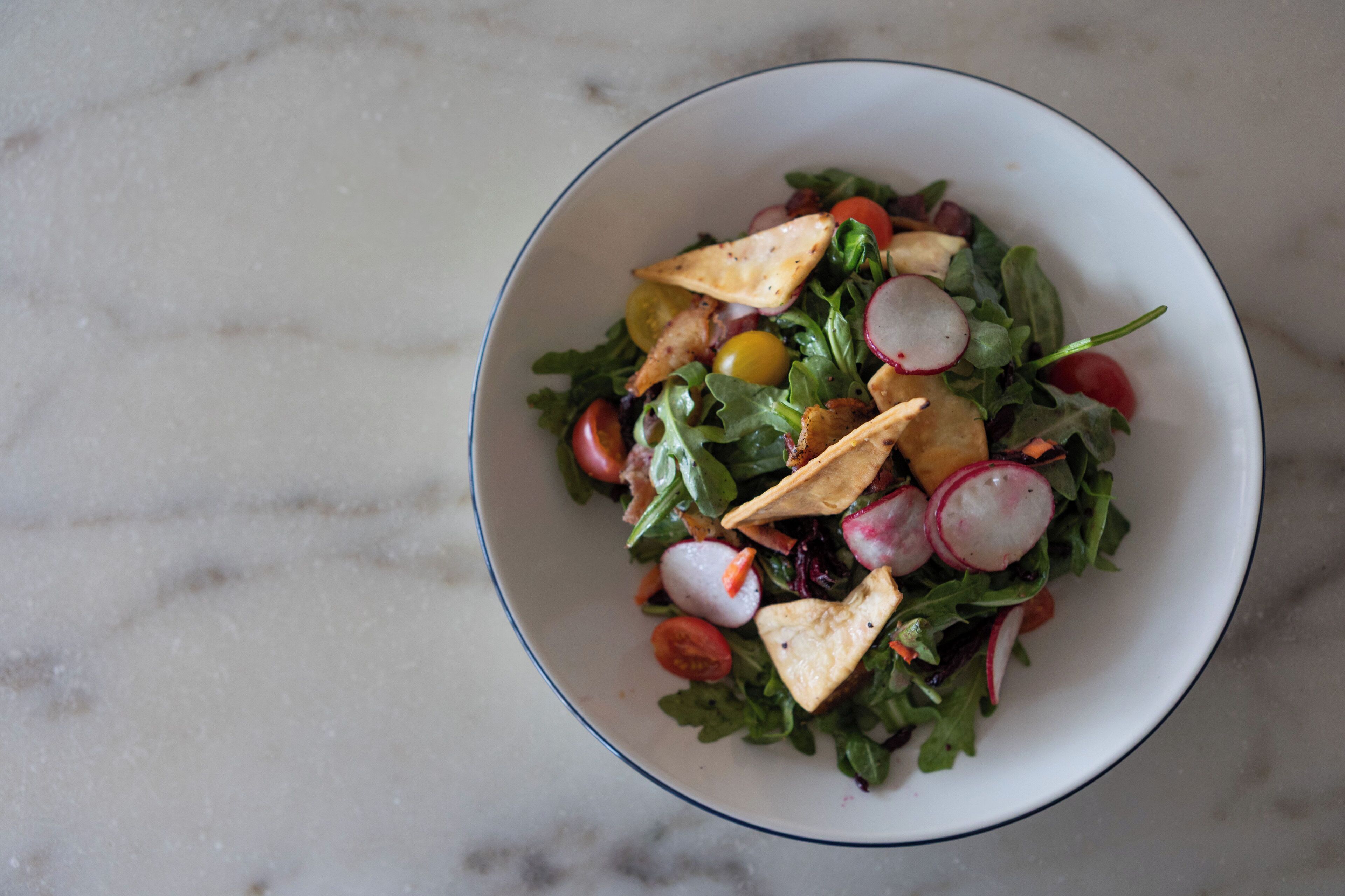A bowl of salad with various vegetables and croutons on a marble surface.