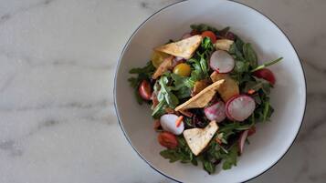 A bowl of salad with various vegetables and croutons on a marble surface.