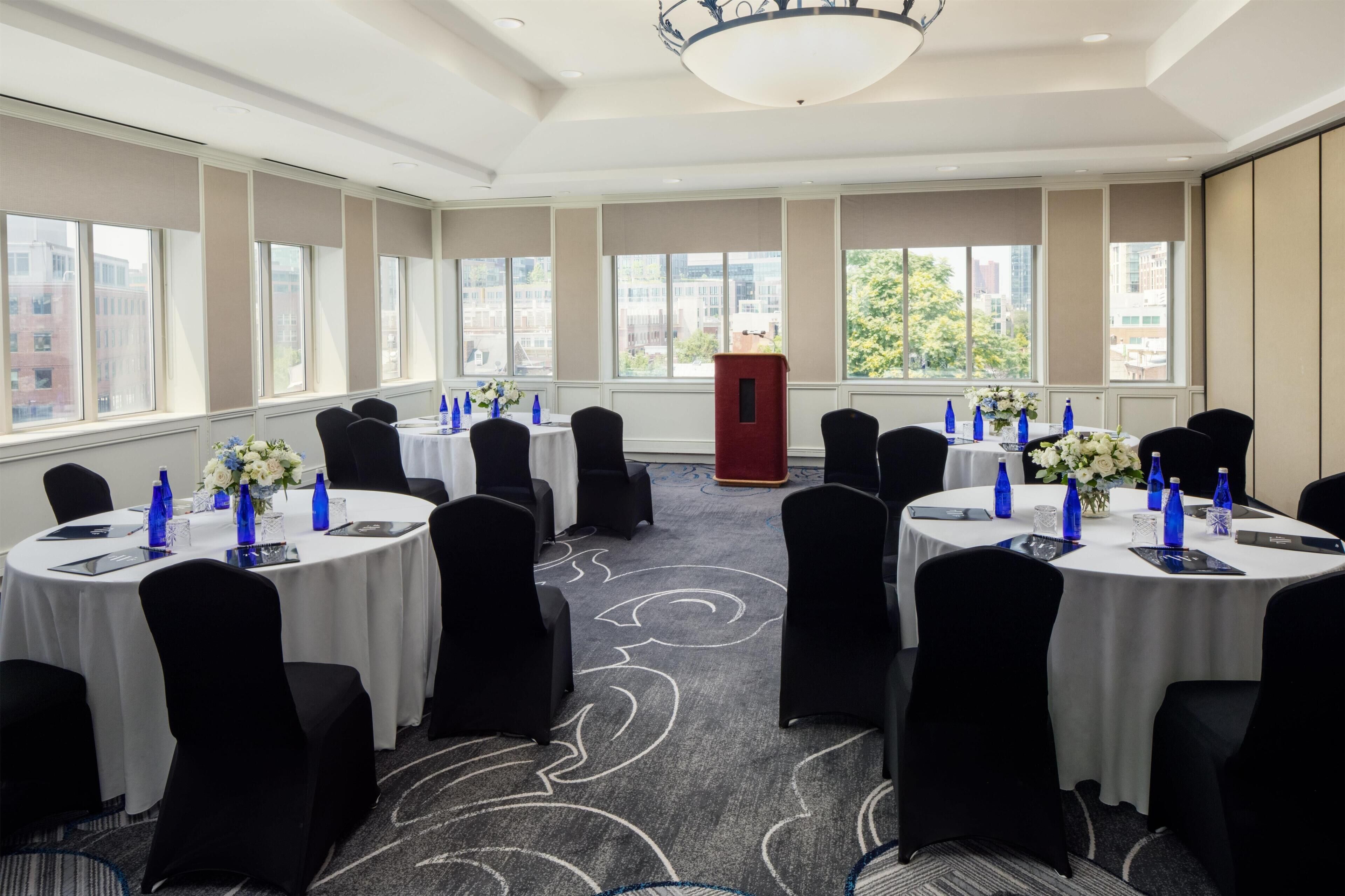 A conference room with round tables, black chairs, and floral centerpieces.