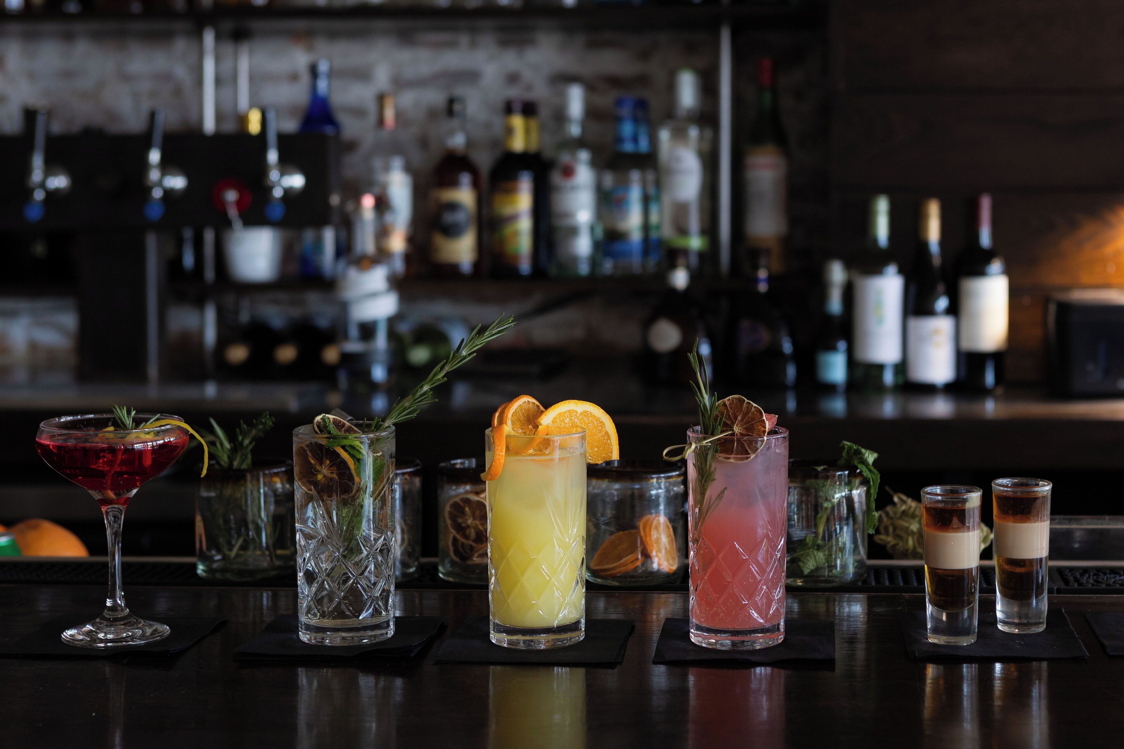 Een bar met diverse drankjes, waaronder cocktails en shotjes, en een selectie flessen op de achtergrond.