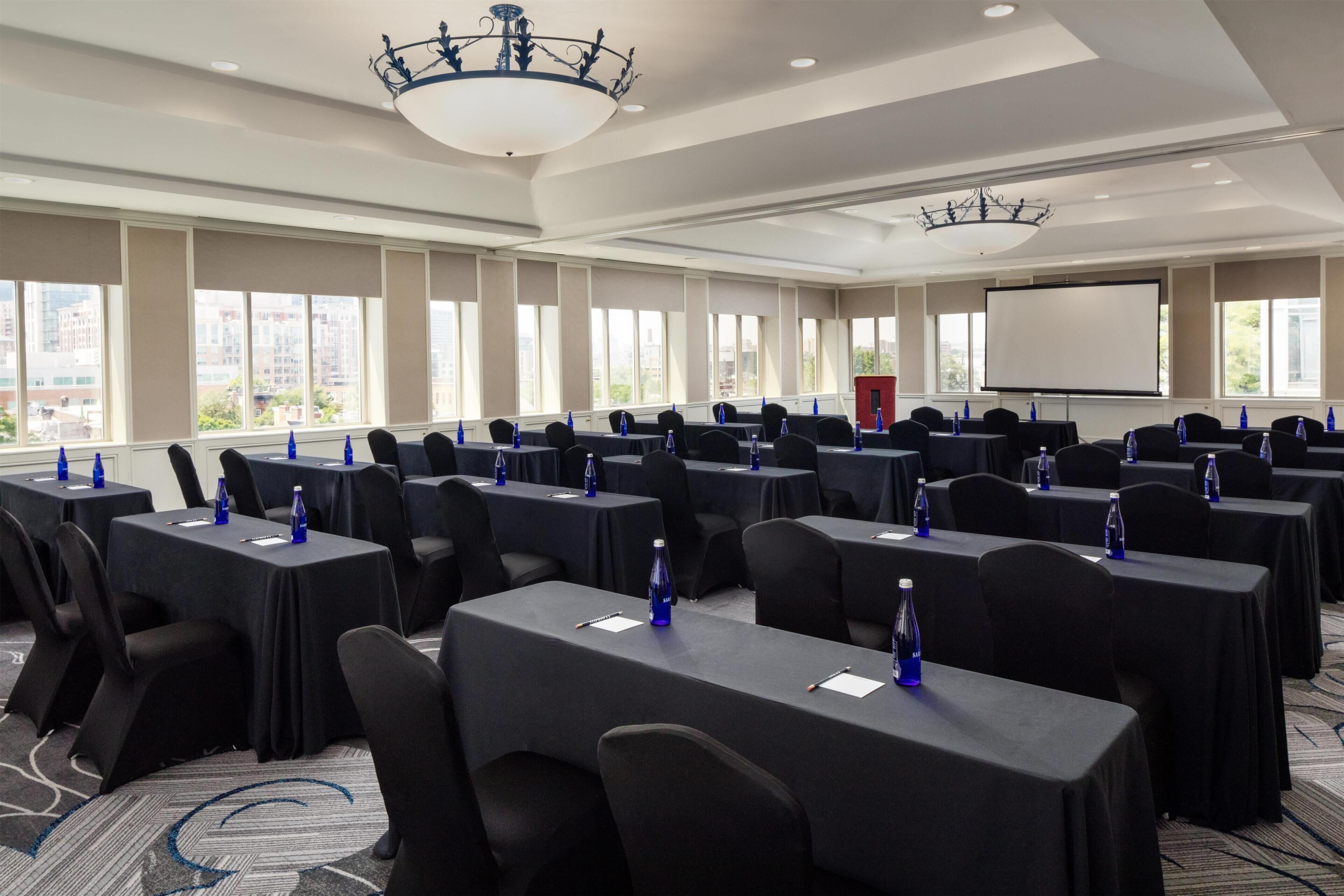 A conference room with multiple tables, chairs, and a projector screen.