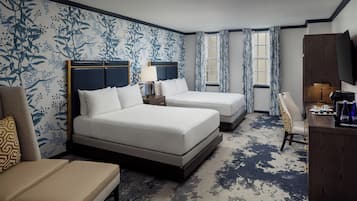 A hotel room with two beds, a desk, a chair, and a TV.